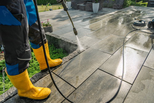 Professional Cleaning of Outdoor Stone Patio Using Pressure Washer and Protective Gear