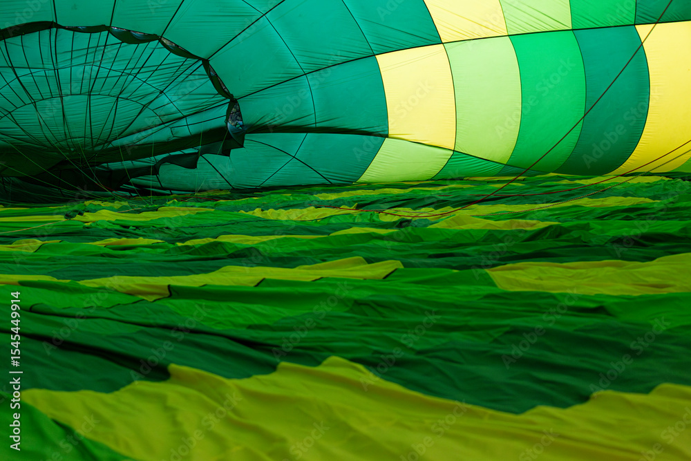 Obraz premium Inside view of a colorful hot air balloon during inflation, with a person in the distance, capturing the anticipation and thrill of adventure travel and ballooning experiences.