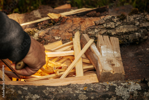 Bilde på lerret A close-up of a person’s hand carefully lighting a fire with small kindling and wood shavings, set between logs on the grass in natural light