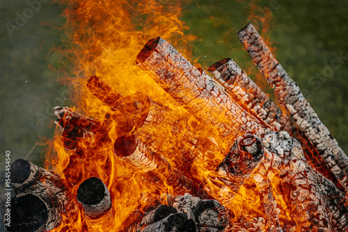 Close-up of a blazing bonfire with charred logs and vivid orange flames, showcasing intense heat and dynamic textures of burning wood.