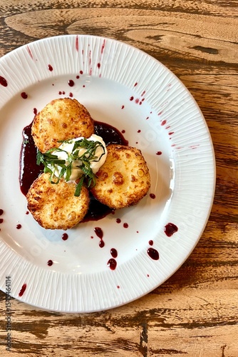 Deliciously plated crispy fritters topped with fresh herbs and creamy sauce, served on a white dish with a rich berry sauce, showcasing culinary artistry and presentation