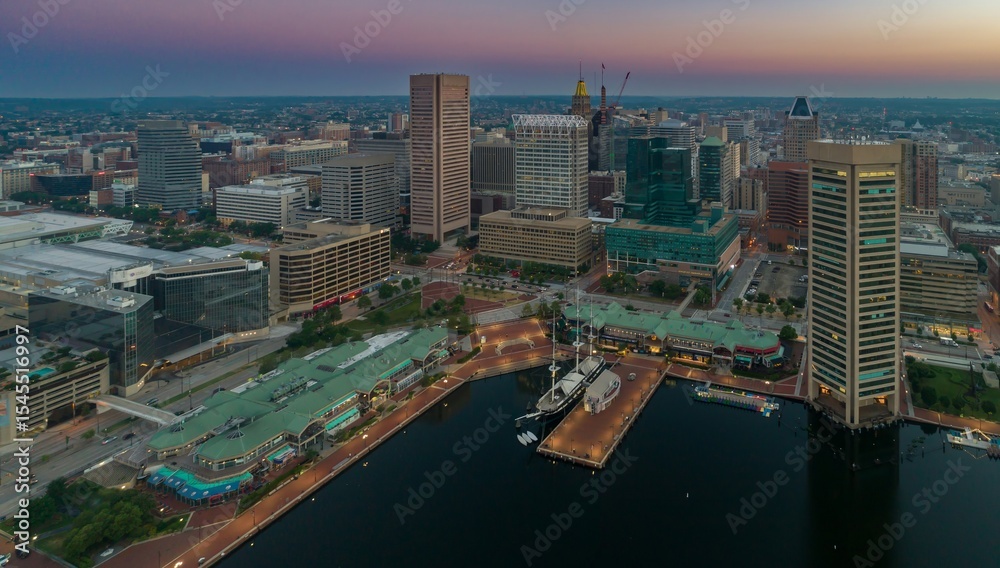 Fototapeta premium Aerial view of Baltimore's Inner Harbor at dusk in the United States. Tall buildings and docked ships create a vibrant cityscape. Tourism and commerce thrive here.
