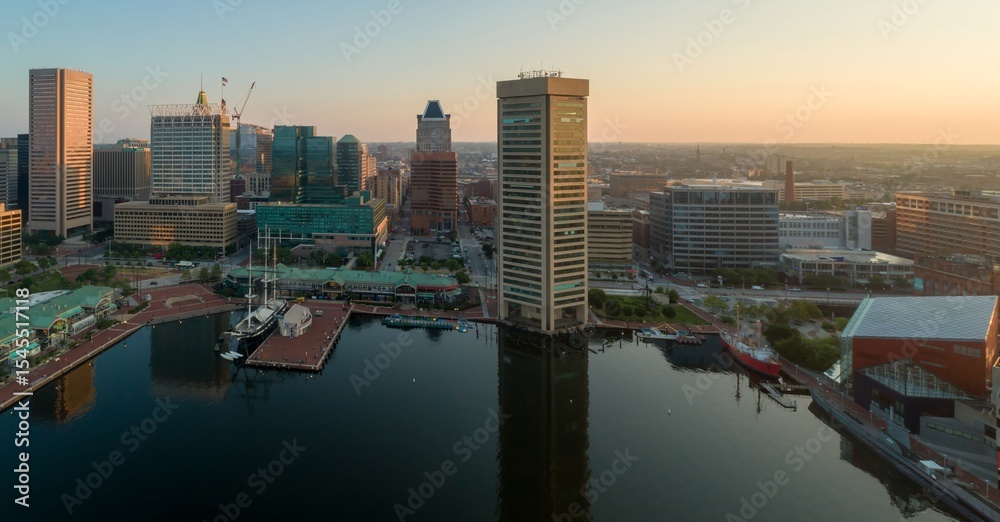 Obraz premium Aerial view of Baltimore's Inner Harbor at sunrise in Maryland, USA. Tall buildings and ships are visible, showcasing the city's skyline and maritime history.