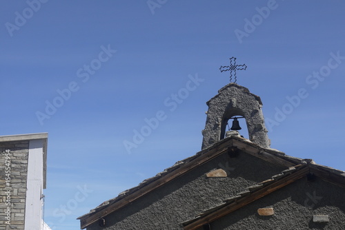 roof of a small church made of stone with bell and a small cross, background with blue sky in summer, Gornergrat, Switzerland