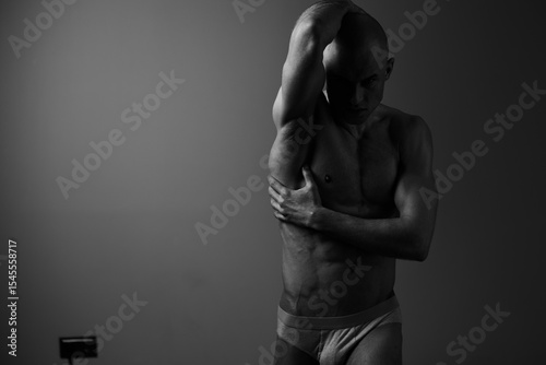 Black and white image of a strong man posing elegantly, showcasing his physique and expression in a dramatic and artistic manner.