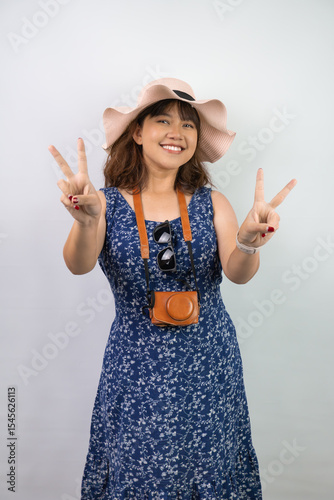 Happy beautiful young asian woman wearing blue summer dress and beach straw hat is showing peace hand gesture or number 2 two, isolated over white background.