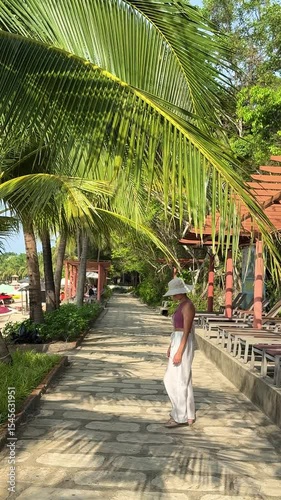Beautiful model girl from Europe walking along the coast in white wide trousers. Posing against the background of the sea and turquoise water.