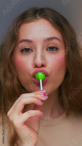 Portrait of Young Woman Eating Sweet Food and Looking at Camera Close Up. Joy of Modern Person with Lollipop Candy on Stick in Hand. Alone Lady Loving and Enjoying Bright Color of Lolly Caramel Treat