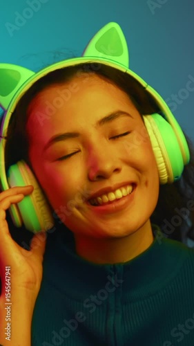 Portrait of Happy Asian Woman in Headphones Listening Music Isolated in Neon Light of Indoors Shot. One Smiling Girl Hears Online Audio of Internet Mp3 Player. Carefree Lady Dancing in Cool Phone Tech