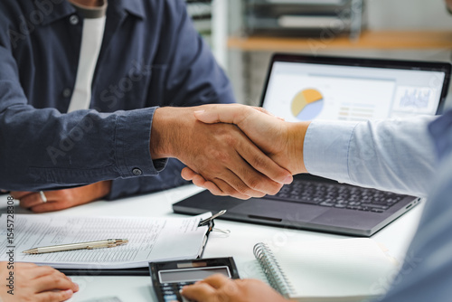 Professional business handshake during financial consultation with advisor, partnership agreement at meeting table with charts and documents
