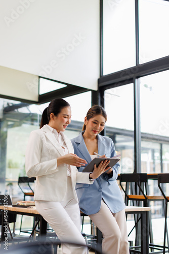 Two Young Asian Happy business women standing and holding tablet in hand confidence leadership in a modern office environment investment market at office.
