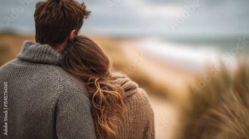 A man and a woman standing on a beach looking out at the ocean