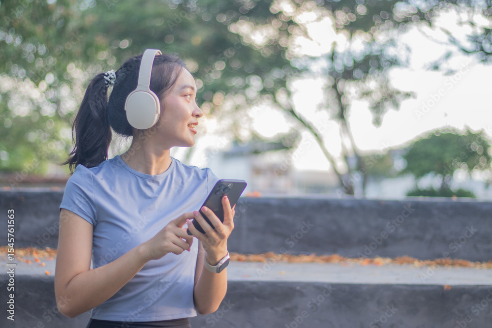 Naklejka premium A smiling young Asian woman jogs outdoors under the spring sunshine, enjoying exercise, independence and well-being. Her energetic movements reflect inspiration, strength and a healthy lifestyle.