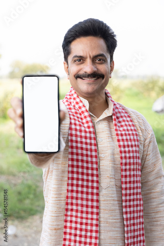 Portrait of smiling mid adult farmer showing smart phone's screen while standing at village.