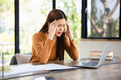  Young asian business woman feeling stress and tired from work sitting on the chair about constant headaches a migraine of working hard at office.