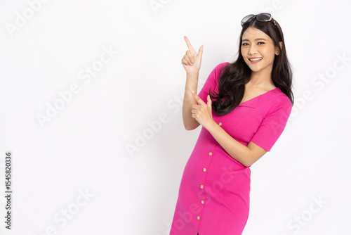 Young Asian woman in pink dress pointing to empty copy space isolated on white background