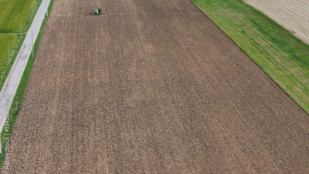 Obraz premium An Agricultural Landscape Depicting Cultivated Land Prepared for Planting with a Tractor at Work in the Distance Adjacent to a Path and Bordered by Greenery