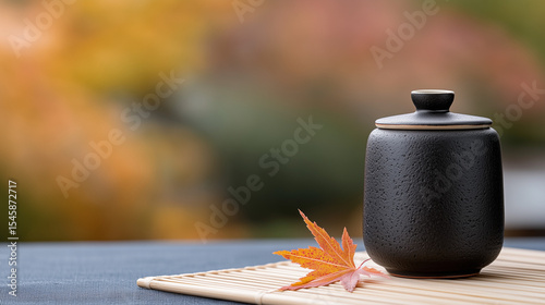 Black ceramic tea canister with autumn leaf on bamboo mat  