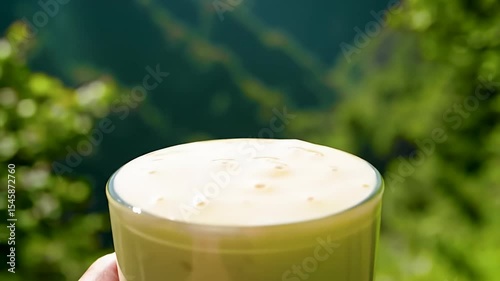 Frothy drink in a glass, outdoor scenery blurred background