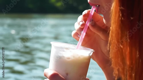 Woman sips drink with pink straw on waterfront, close-up