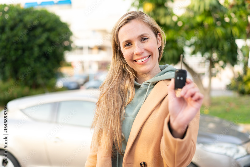 Fototapeta premium Young blonde woman holding car keys at outdoors with happy expression