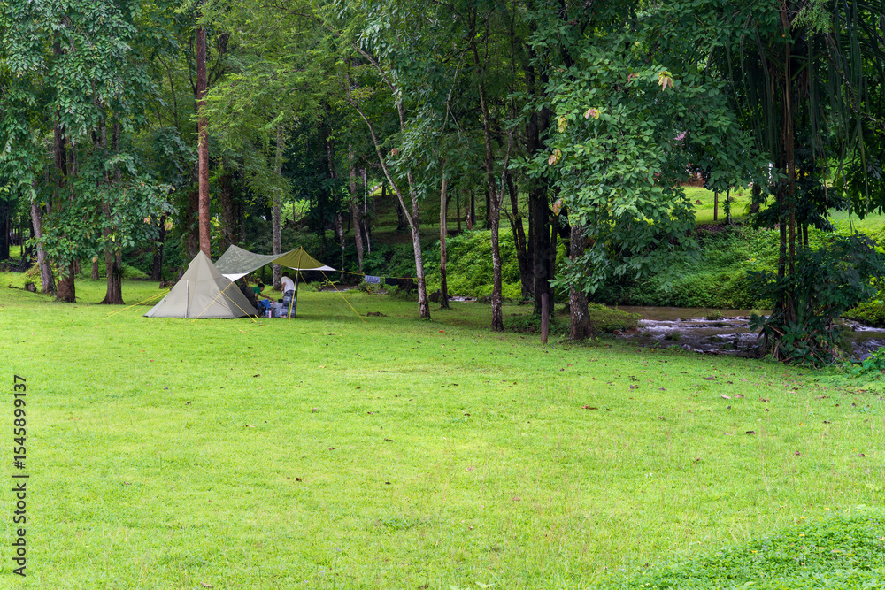 Fototapeta premium nature camping or glamping cabin tent on green grass lawn campground with water stream shady and tree garden with camper family holiday vacation at khao laem national park in ka teng cheng waterfall