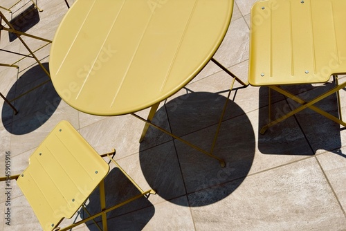 Bright yellow round table and foldable chairs on a terrace in Malta in a play of light and shadow.