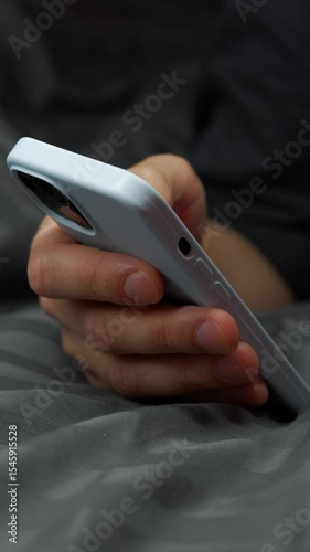 A man lies on a gray bed in the room with a phone in his hands, reads the news and texts someone.
A touchscreen phone in a blue case close-up