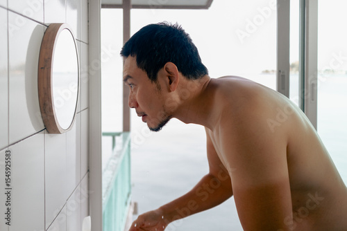 Man washing his face in front the mirror in the bathroom in the morning with view.