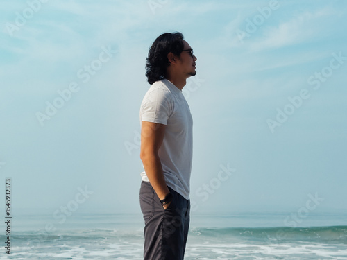 Man wears white t-shirt and sunglasses enjoy walking on the beach.