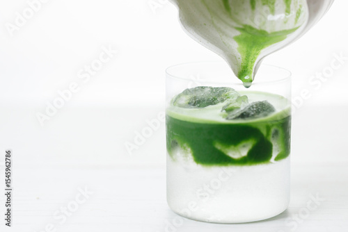 fresh matcha tea, green tea pouring on a glass of coconut water on white wooden table.