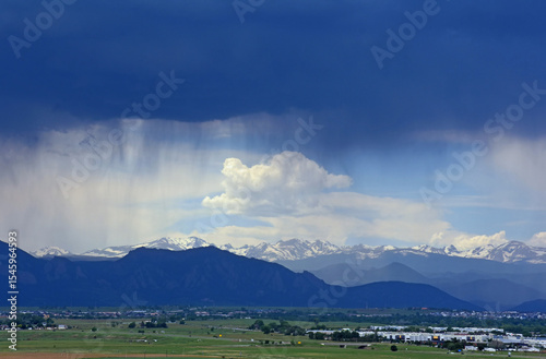 looking out at prairie and  the virga clouds of an afternoon thunderstorm in  the snow-capped peaks of the front range of the colorado rocky mountains, as seen from broomfield, colorado 