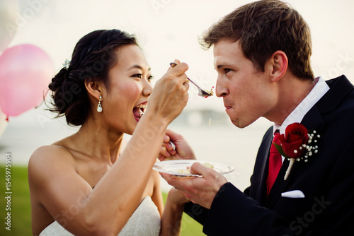 Happy bride and groom feeding each other cake at their wedding reception. Candid moment capturing joy and celebration.