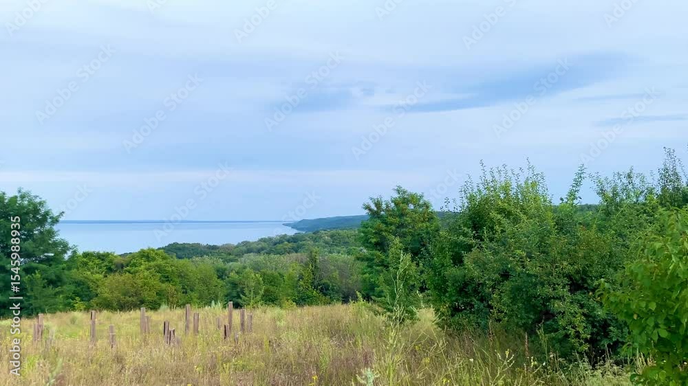 Scenic landscape overlooking the Kaniv Reservoir in Cherkasy region, with grassy fields, scattered trees, and a calm blue horizon under a soft skyю Scenic landscape overlooking the Kaniv Reservoir in Cherkasy region, with grassy fields, scattered trees, and a calm blue horizon under a soft skyю