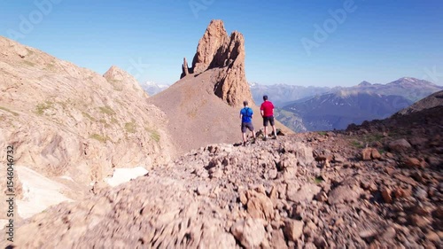 Aerial 4K drone footage of two hikers admiring Agujas de Lavasar in the Pyrenees of Aragón, rocky alpine landscape in Chistau Valley with epic mountain peaks and dramatic geological formations
