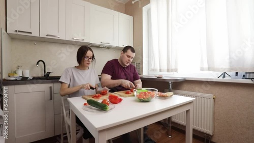Vegetable salad preparation in home kitchen by couple sitting at dining table.