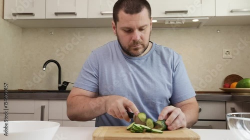 man cutting cucumber in the kitchen, middle-aged person cooking dinner, modern recipe with fresh vegetables