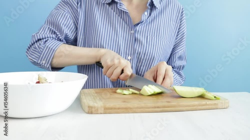 Woman cutting apple with knife on blue background, lifestyle of healthy cooking at home, fresh ingredients for a balanced diet.