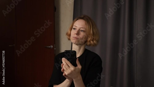 Angry woman with phone at home, experiencing solitude, reflecting on feelings of disappointment and sorrow.