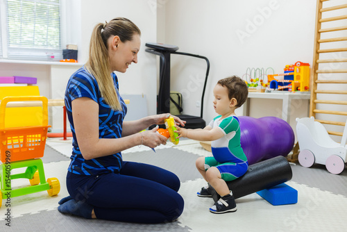 Female physical therapist training a young child in physical skills of standing up and sitting down during a rehabilitation session at the center