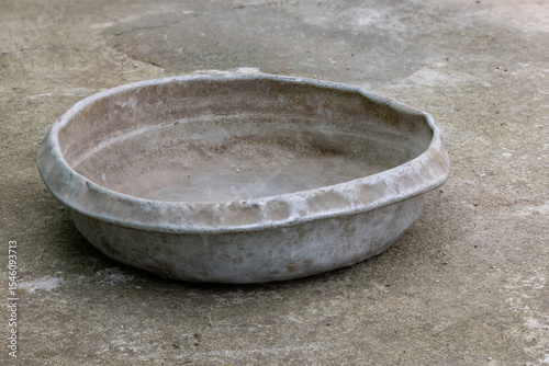 Weathered dented gray aluminum basin on concrete floor