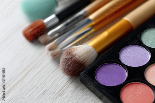 Flat lay of colorful eyeshadow palettes with brushes and makeup tools on light wooden surface