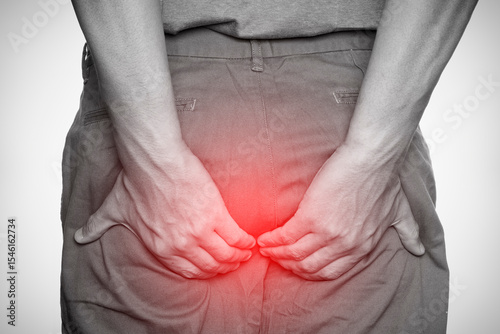 Man clutching buttocks in pain with red spot highlight, concept of hemorrhoids or anal discomfort, isolated on white background.