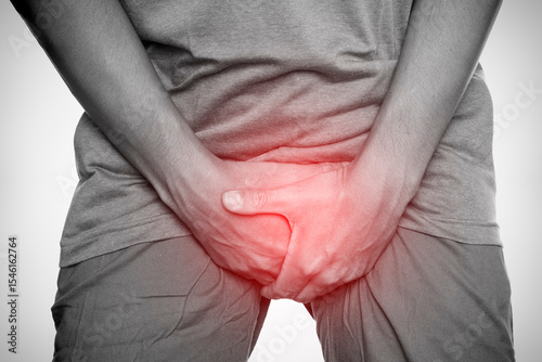 Slika na platnu Man clutching groin area in pain with red highlight, indicating genital discomfort or urological problem, isolated on white background