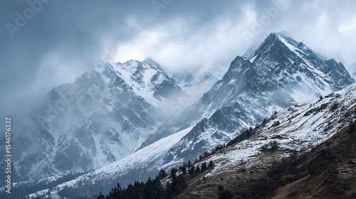 Dramatic snow-capped mountains landscape, clouds and fog covers stone slopes