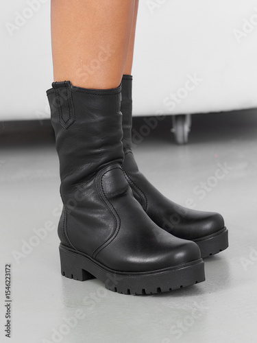 Black leather boots with thick platform soles and stitching details, worn by a person with the lower legs visible. The footwear appears sturdy and stylish, suitable for various outfits