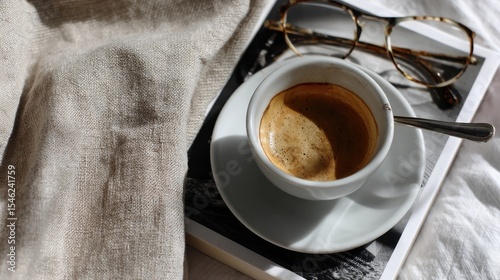 Minimal cozy morning scene with espresso coffee cup, vintage eyeglasses and magazine on linen fabric, symbolizing slow living, relaxation, and lifestyle aesthetics.