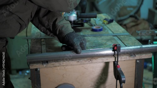 Workshop. The worker removes the clamps that were holding the cut steel pipe on the workbench and examines it.