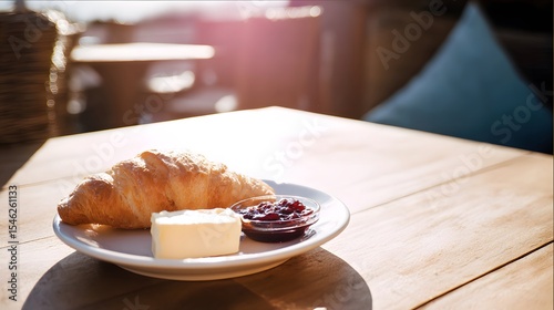 Croissant with butter and jam on a cafe table under soft sun