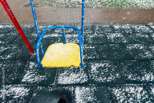 Colorful swing covered in snow during a winter snowfall in a playground near a city park
